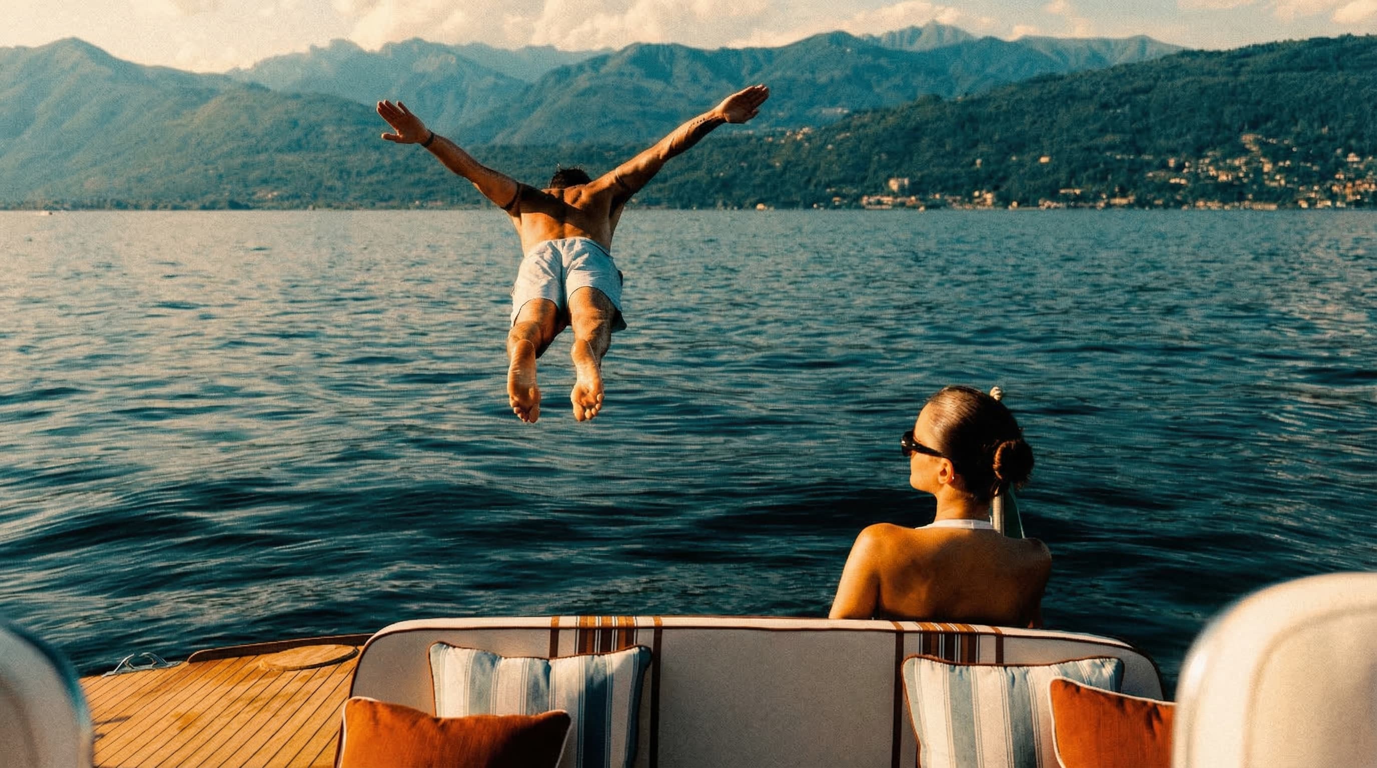 Man diving off a yacht into a lake while a woman watches, joyful and free
