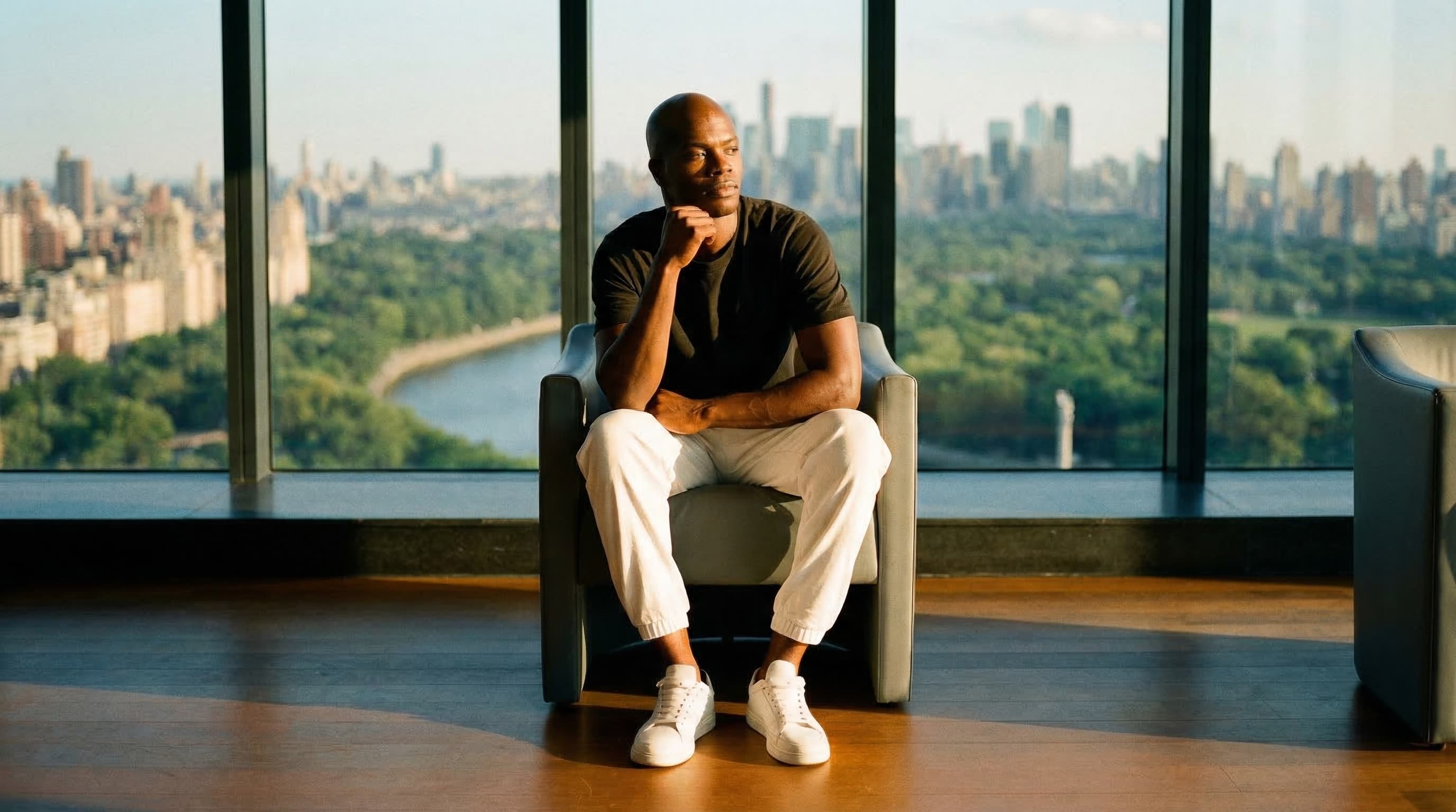 Man sitting in a chair with a city skyline behind him — confident and composed